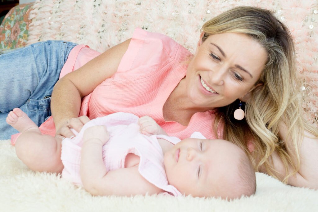 Elaine Harvey providing gentle sleep support as she lies beside a peacefully sleeping baby on a soft, floral-patterned bed