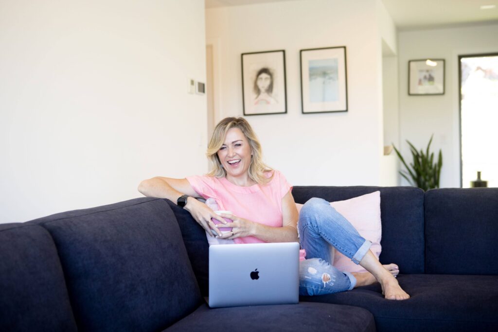 “Elaine Harvey offering gentle sleep support in a virtual consultation, smiling with her laptop on a cozy couch.