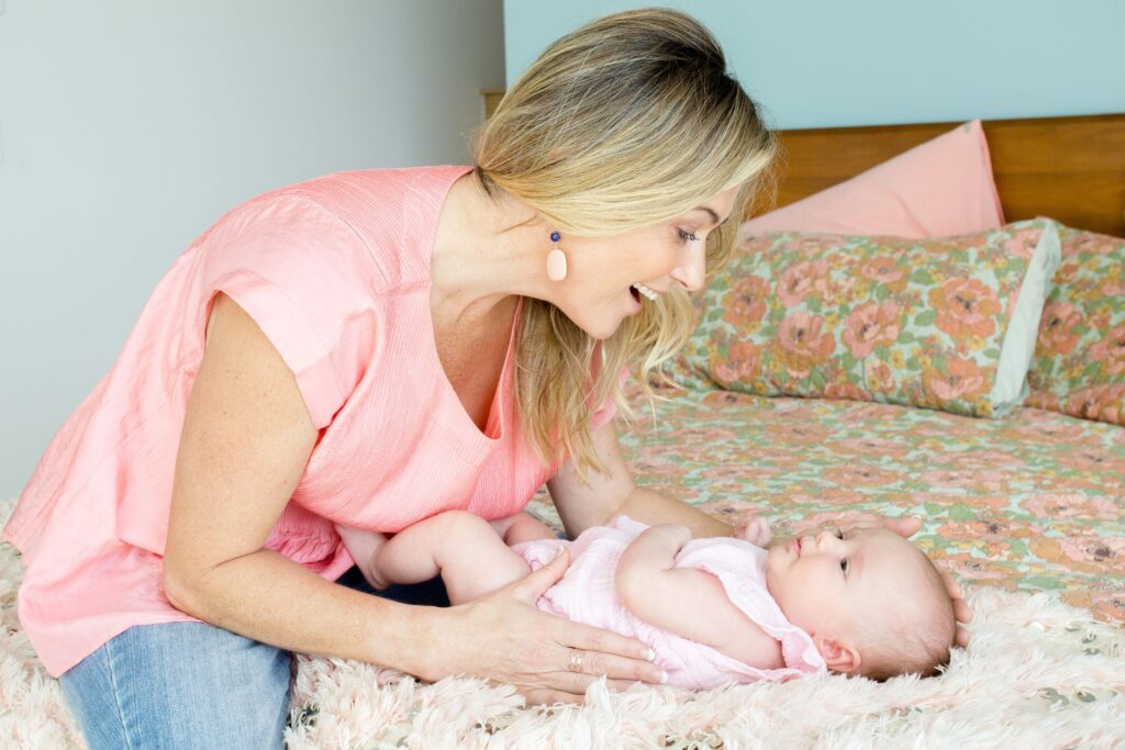 Elaine Harvey providing gentle sleep support as she soothes a baby resting on a soft, floral-covered bed.