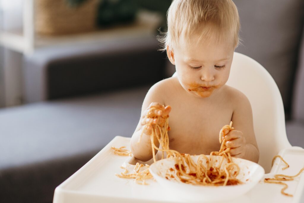 Baby exploring spaghetti with hands and face during a messy mealtime—part of the baby-led and spoon-fed weaning journey.