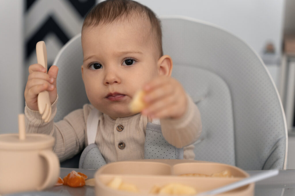Baby self-feeding with finger foods during a baby-fed and spoon-fed weaning routine.